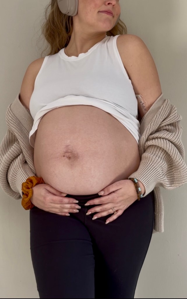 Pregnant woman wearing headphones and loungewear cradling her belly during a difficult third trimester.”